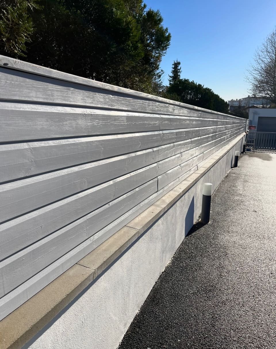 Clôture bois repeinte en gris clair sur murette enduite fraîchement remise en peinture, à Tarnos