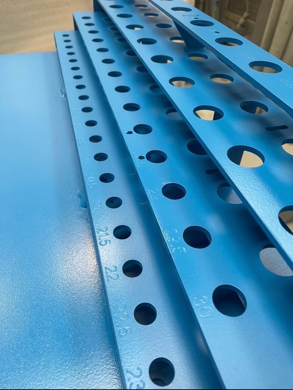 Rails métalliques perforés fraîchement laqués en bleu, posés en atelier après mise en peinture